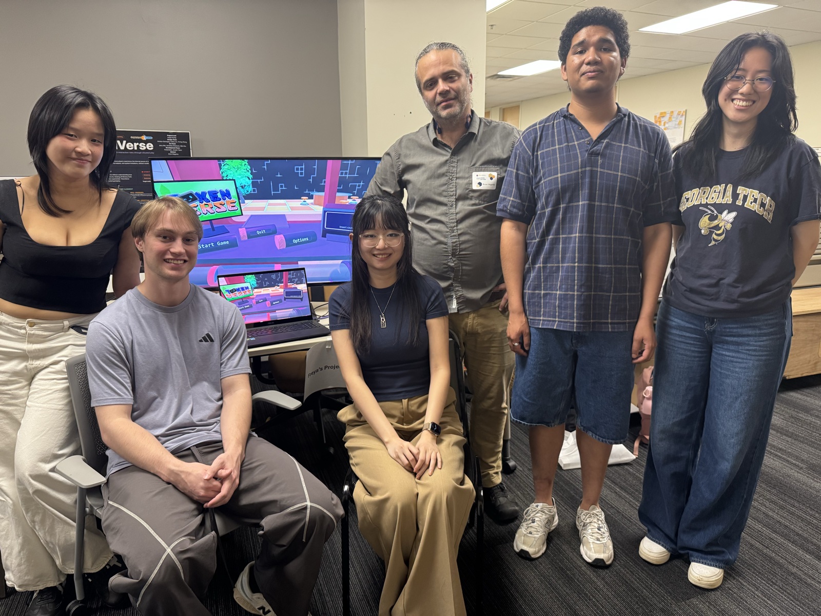 The TokenVerse team posing together at Demo Day, with the game running on a monitor behind them